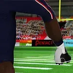 En fodboldspiller i mørkt tøj sparker en amerikansk fodbold på en grøn bane foran publikum og målstolper