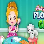 En tegning af en pige i en lyserød kjole med en krone, som sidder ved et bord med en hvid kat ved siden af og forskellige små genstande på bordet, med teksten Baby Hazel Flower Girl i baggrunden