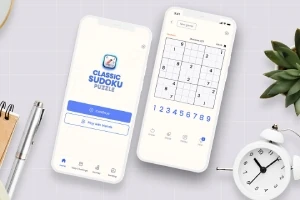 To smartphones vises med en Sudoku-app åben, omgivet af en urteplante, en metalpen og et hvidt vækkeur på en grå baggrund