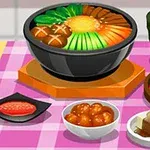 En række asiatiske retter, inklusive en stor skål med suppe og grøntsager, flere små retter og en grøn drik, placeret på en ternet pink dug