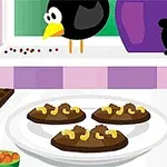 En tallerken med fire chokoladekager pyntet med nødder, omgivet af ingredienser som chokolade og krydderier, med en sort fugl i baggrunden