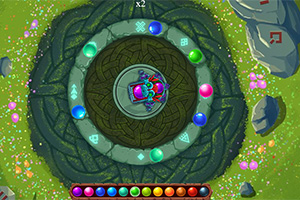 Farverig spiral med kugler arrangeret omkring et centralt mønster på en grøn, blomstret baggrund med sten