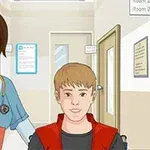En kvindelig sygeplejerske med stetoskop står ved siden af en mandlig patient i kørestol på en hospitalsgang