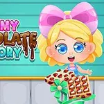 Blond pige med stor lyserød sløjfe holder en chokoladeæske foran en blå stribet baggrund, ved siden af teksten Yummy Chocolate Factory